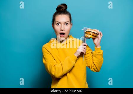 la ragazza mostra lo shock misurando l'altezza dell'hamburger con un calibro sul lato di se stessa Foto Stock