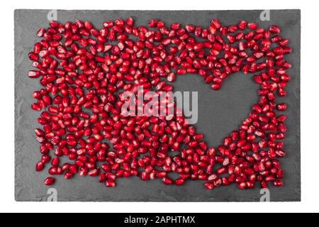Festive sfondo romantico per il saluto di San Valentino post-card. I semi di melograno rosso sulla tavola di pietra sono disposti nella forma del simbolo di cuore dell'amore Foto Stock