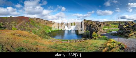 Epica vista panoramica dei droni aerei che volano sul paesaggio della cascata Hjalparfoss e della laguna in una giornata di sole. Foto Stock