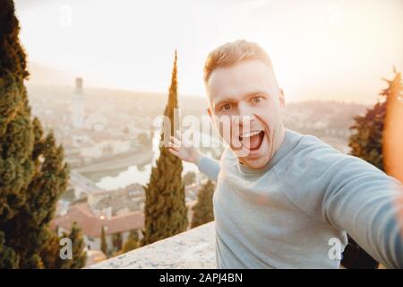 Uomo felice traveler tenendo selfie foto su sfondo città Verona Italia tramonto. Concetto di viaggio Foto Stock
