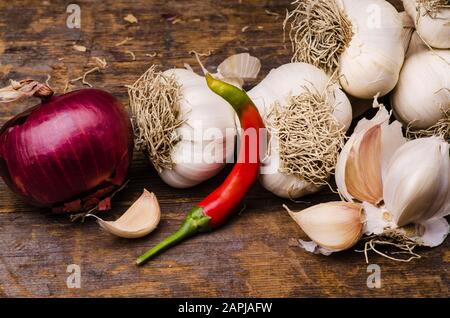 Trecciato aglio secco, una cipolla rossa e peperoncino piccante su rustico tavolo in legno. Ancora vita Foto Stock