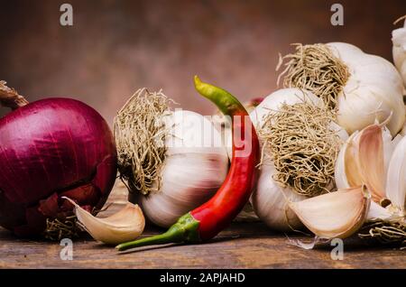 Trecciato aglio secco, una cipolla rossa e peperoncino piccante su rustico tavolo in legno. Ancora vita Foto Stock