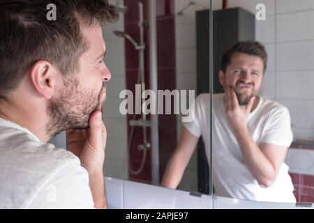 L'uomo controlla le condizioni della sua pelle in riflessione specchio in bagno Foto Stock