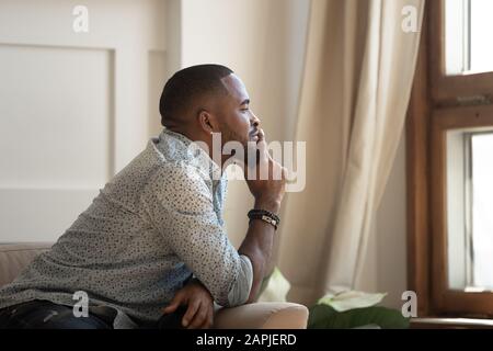 Uomo africano pensoso seduto sul divano che guarda fuori la finestra Foto Stock