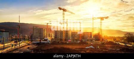 Grande cantiere con diverse gru che lavorano su un complesso edilizio, illuminato dalla luce solare calda dell'oro Foto Stock