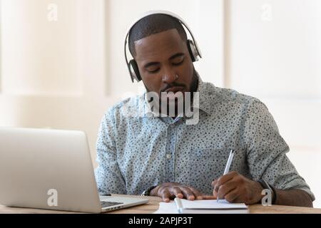 Gli studenti africani che indossano le cuffie ascoltano il corso audio fa appunti Foto Stock