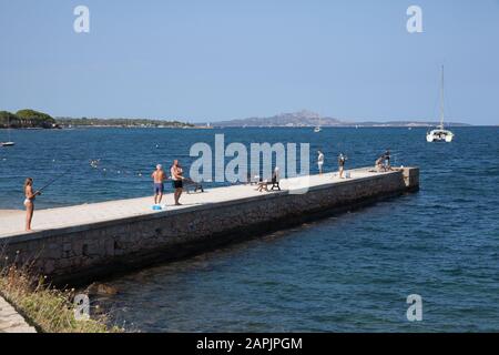 Persone che pescano al largo del molo sulla spiaggia di Cannigione, Sardegna, Italia Foto Stock