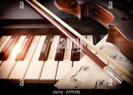 Arco violino e musica a fogli sui tasti piano. Concetto di interpretazione della musica da pianoforte e degli strumenti a corda. Vista frontale. Composizione orizzontale. Foto Stock