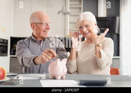 Funny foto di Coppia matura mettendo moneta nel salvadanaio a casa. Risparmi, piano pensionistico concept Foto Stock