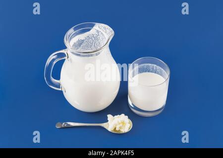 In casa bevanda fermentata kefir versando in un bicchiere in un quartiere alla moda di sfondo blu, concetto di fermentazione naturale cibo e salute intestinale Foto Stock