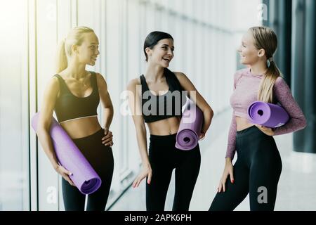 Gruppo di giovani ragazze sportive con stuoie yoga in piedi in palestra. Compagni femminili in palestra riposati dopo il fitness Foto Stock