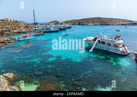 Comino, Malta, 15 giugno 2019: Splendida laguna blu con acque turchesi, yacht e barche con vacanzieri e bagnanti in un'estate soleggiata Foto Stock