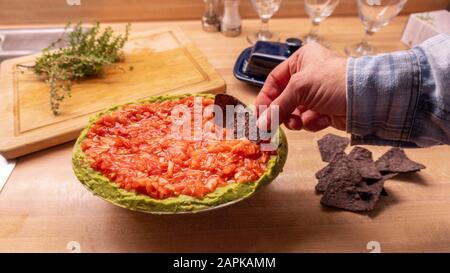 Un uomo medio anziano e informale che si tuffa nella salsa messicana mentre tiene i chip nacho tortillia Foto Stock