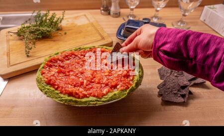 Ragazza informale che si tuffa in salsa messicana mentre tiene i chip nacho tortiglia Foto Stock