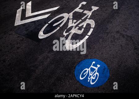 Marcature del percorso del ciclo su uno sfondo nero di asfalto visto da un'angolazione elevata. Due simboli e frecce di direzione della bicicletta diversi, segnaletica stradale.