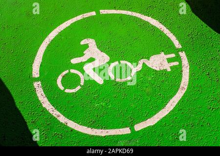 Parcheggio per motociclette elettriche con cartello della stazione di carica verniciato su asfalto. Simbolo bianco di una motocicletta con presa su sfondo verde. Foto Stock
