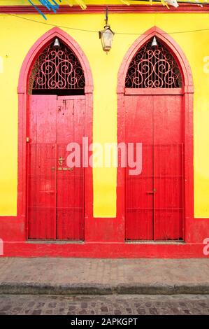 Luminosa vista di porte rosse dai colori vivaci con cime appuntite insieme su parete gialla a Olinda, Brasile Foto Stock