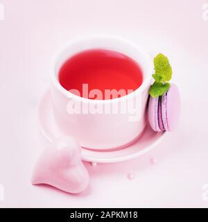 Tè alla frutta, blackberry macaroon o macaron e cuore di ceramica rosa su sfondo rosa pallido, copia spazio Foto Stock