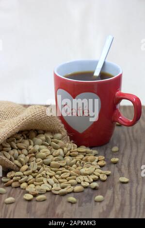 Una tazza di caffè accanto a un caffè in un sacco di burlap su un tavolo di legno e sfondo bianco con spazio per i testi. Spazio di copia Foto Stock