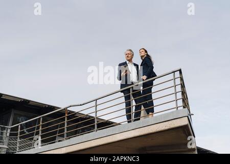 Uomo d'affari e donna d'affari che si trovano su un balcone all'esterno dell'edificio dell'ufficio Foto Stock