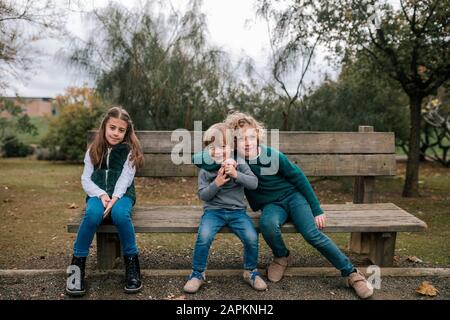 Foto di gruppo di tre bambini seduti su panca di legno all'aperto Foto Stock