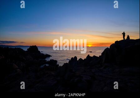 Italia, Provincia di Sassari, Santa Teresa Gallura, Silhouette di coppia ammirando il tramonto sul Mar Mediterraneo dalla cima di Capo testa Foto Stock