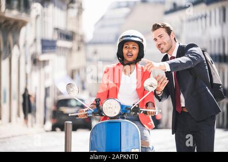 Uomo d'affari con telefono cellulare che parla con la donna su scooter a motore in città, Lisbona, Portogallo Foto Stock
