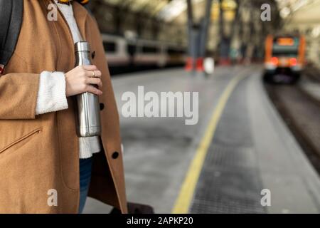 Primo piano della donna che tiene thermos alla stazione ferroviaria Foto Stock