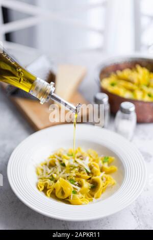 Olio d'oliva che si versa in piatto di tortellini italiani con formaggio grana Foto Stock