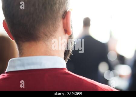 dietro la vista di un giovane uomo con la barba ad un raduno Foto Stock