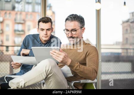 Uomo d'affari maturo con tablet e giovane che lavora in ufficio Foto Stock