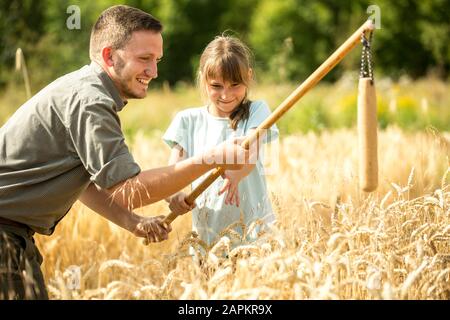 I bambini che imparano come flail grano in campo Foto Stock