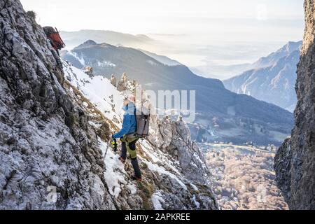 Alpinista in piedi in una montagna rocciosa innevata guardando in alto, Orobie Alpi, Lecco, Italia Foto Stock