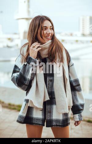 Giovane donna bruna con cappotto e sciarpa bianchi e neri in città Foto Stock