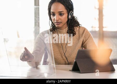 Giovane donna d'affari seduto alla scrivania in ufficio utilizzando uno schermo trasparente Foto Stock