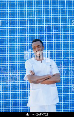 Ritratto di medico ridente che si levano in piedi contro il muro di tegole blu Foto Stock