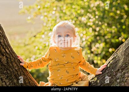 Ritratto di bionda ragazza toddler seduta su tronco d'albero tirando facce divertenti Foto Stock