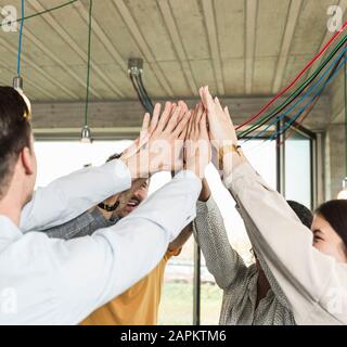 Giovani uomini d'affari felici che alzano le braccia in ufficio Foto Stock