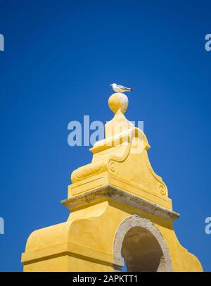 Scatto ad angolo basso di un gabbiano appollaiato sulla cima di una torre gialla sotto il cielo azzurro Foto Stock