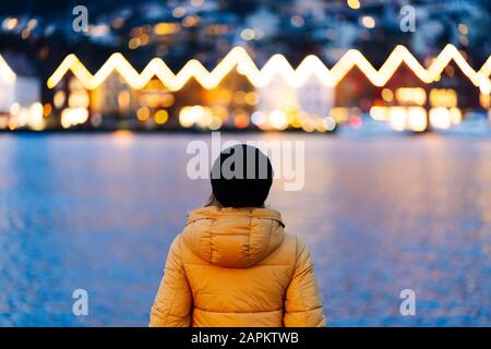 Vista posteriore della donna che indossa una giacca gialla e che si trova nel porto di Bergen, Norvegia Foto Stock
