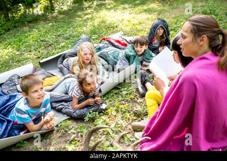 Insegnante di lettura storia per i bambini a scuola, campeggio nella foresta Foto Stock