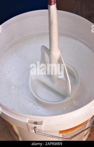 Qualcuno rimuove il contenuto di una benna di vernice bianca con uno shaker di vernice Foto Stock