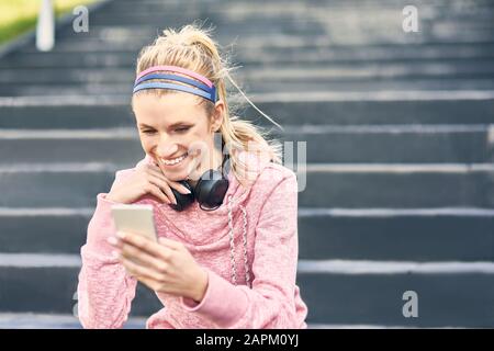 Donna sportiva seduto sulle scale, utilizzando lo smartphone Foto Stock