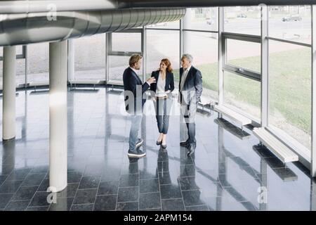 Gli uomini d'affari che parlano alla finestra in un moderno edificio d'ufficio Foto Stock