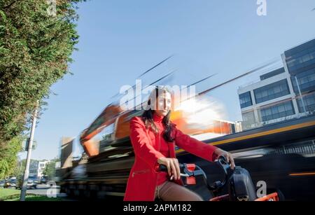Giovane donna in bicicletta a noleggio nel traffico della città Foto Stock