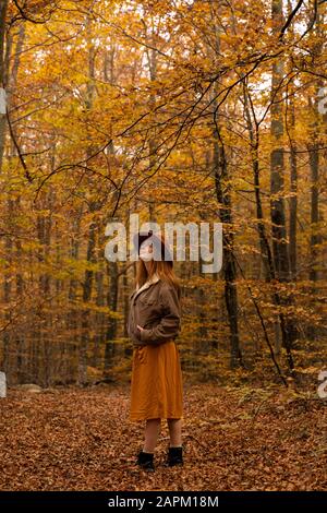 Giovane donna alla moda rossa che esplora la foresta autunnale Foto Stock