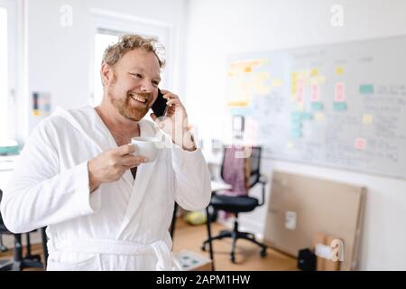 Uomo d'affari con accappatoio in ufficio che parla al telefono Foto Stock