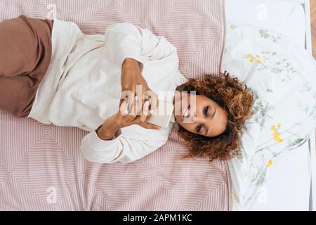 Giovane donna sdraiata a letto utilizzando uno smartphone Foto Stock