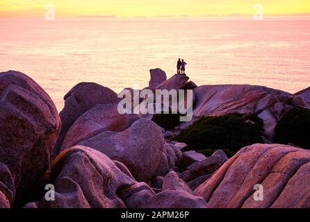 Italia, Provincia di Sassari, Santa Teresa Gallura, Silhouette di coppia ammirando il tramonto sul Mar Mediterraneo dalla cima di Capo testa Foto Stock