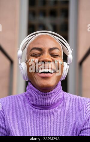 Ritratto di donna dai capelli bianchi con cuffie bianche e adesivi sul suo viso ascoltando musica e ridendo Foto Stock